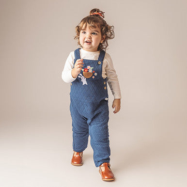 Toddler girl in denim overalls with floral embroidery and brown leather shoes.