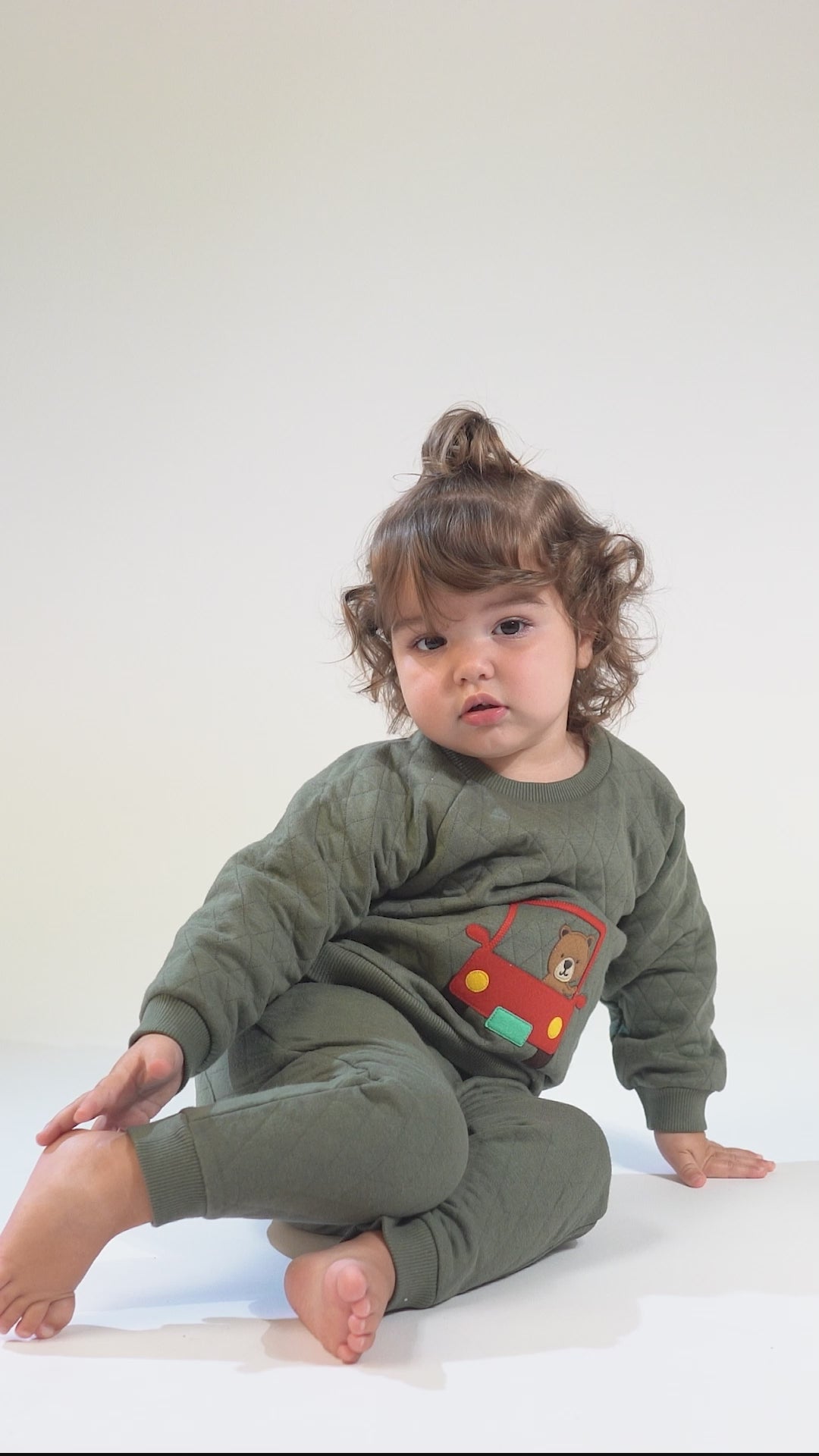 Baby in an olive-green quilted tracksuit with a red car and brown bear embroidery.